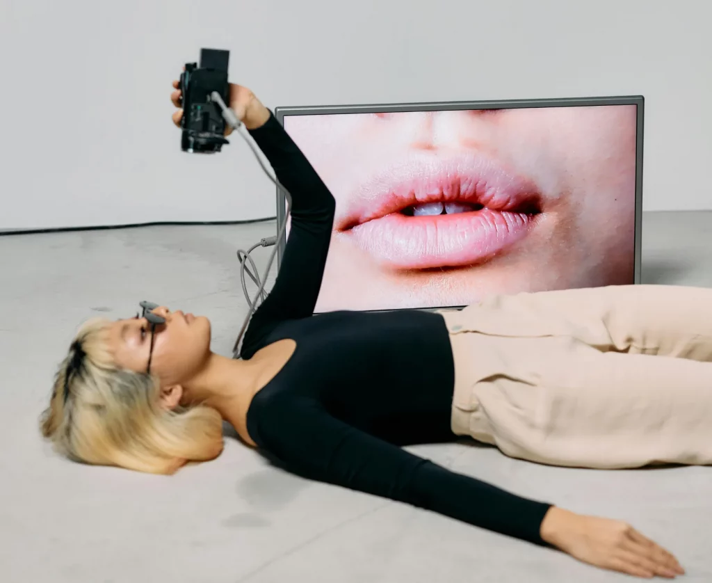 Editorial-style content creation with woman holding a camera while lying in front of a screen displaying lips, symbolising Marketing Valley’s bold creative approach.