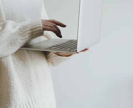 Person in cream knit sweater working on a laptop, symbolising Marketing Valley’s creative and strategic social media workflow.